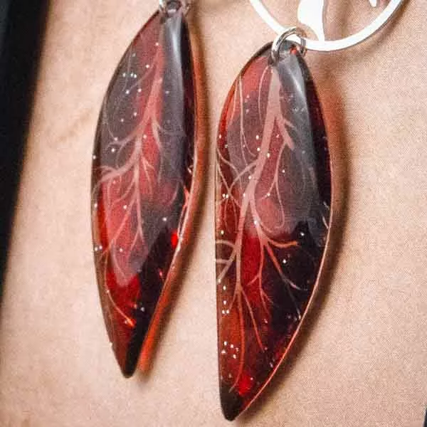 Gros plan des boucles d’oreille arbre de vie et ailes de fée rouges