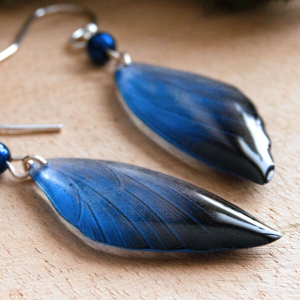 Gros plan des boucles d’oreilles ailes de fée Cléophée en résine bleu translucide et perle nacrée.