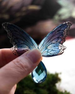 Ailes de fée bleues de Lioraëlys tenues à la main, traversées par la lumière