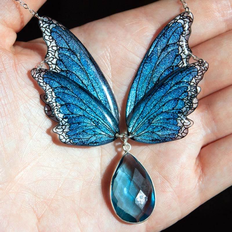 Bijou ailes de fée bleu Lioraëlys dans une main, sous la lumière du soleil