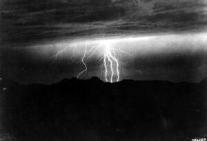 Éclair frappant une montagne dans la nuit, évoquant la tempête de la naissance de Merlin