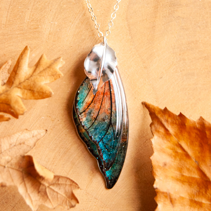 Sautoir Feu Follet fabriqué avec les ailes de la fée Sylmeria, présenté dans un décor naturel