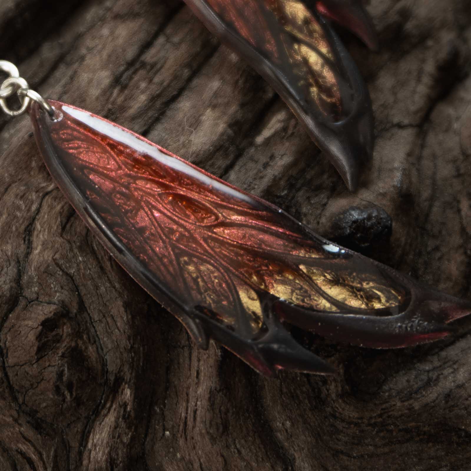 Gros plan sur une aile des boucles d'oreilles Morgane Élégance, montrant les nervures en relief, les reflets cuivrés et or et les bordures noires.