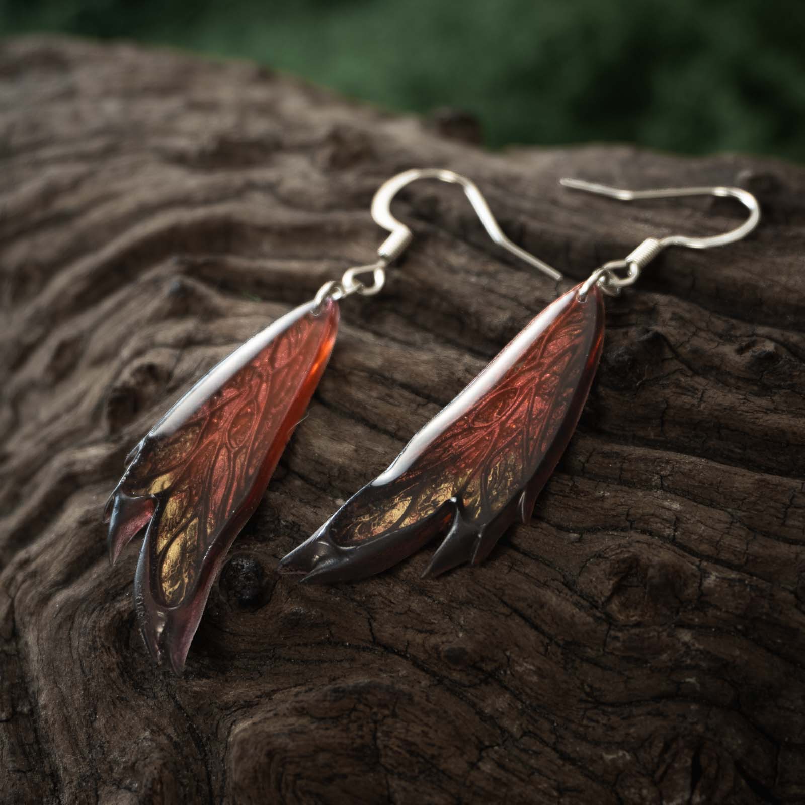 Paire de boucles d'oreilles Morgane Élégance posées sur une souche de bois sombre, aux nuances rouge cuivré, or et noir.