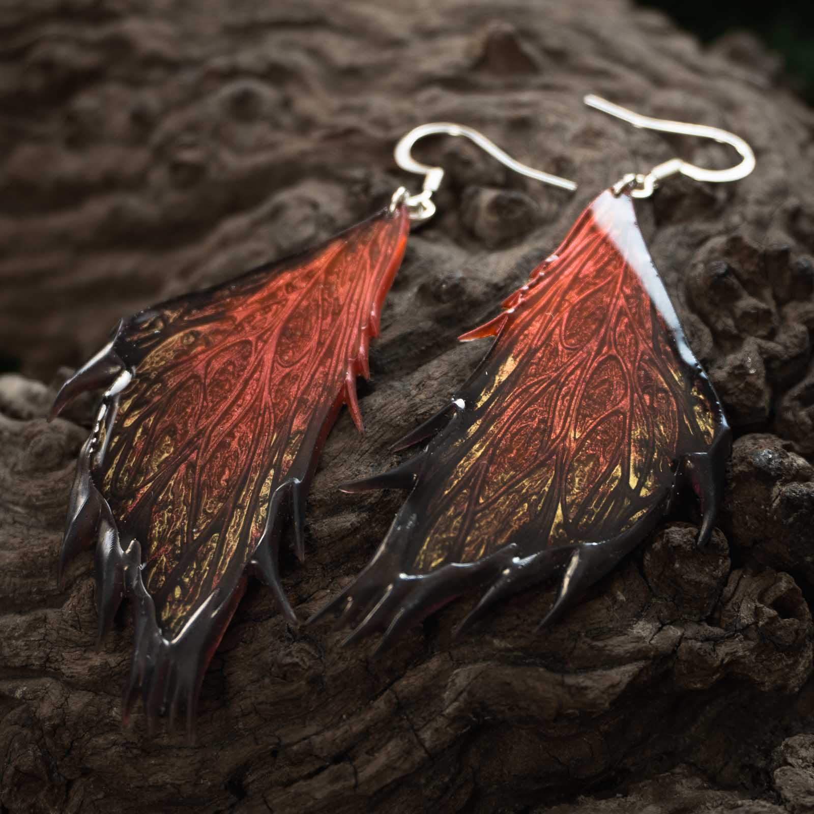 Boucles d'oreilles Morgane Prestige - Sur bois Paire de boucles d'oreilles Morgane Prestige posées sur une souche de bois sombre, révélant les nuances rouge cuivré, noir et or des ailes de fée.