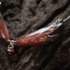 Gros plan sur une aile du collier Morgane Élégance, ses nervures en relief aux reflets cuivrés et or, et son grenat rouge profond.