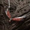 Collier Morgane Élégance posé sur une souche de bois sombre, avec ses ailes de fée rouge cuivré aux contours noirs et son pendentif en grenat central.